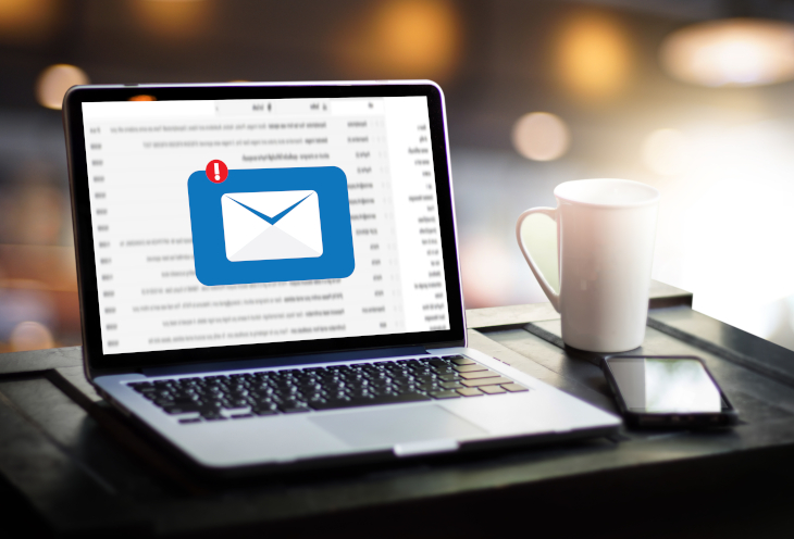 There is an open laptop, smartphone and mug on the desk. The screen shows a missed email
