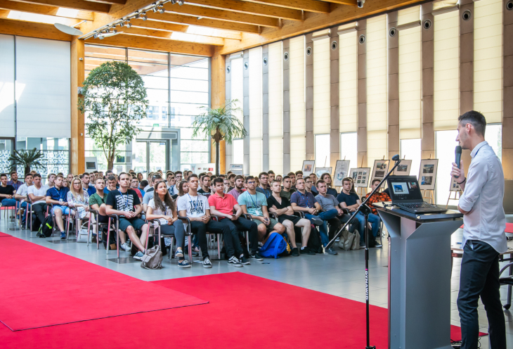 Students sit in the auditorium and listen to the lecture opening the summer IT internship. A man stands behind a desktop 