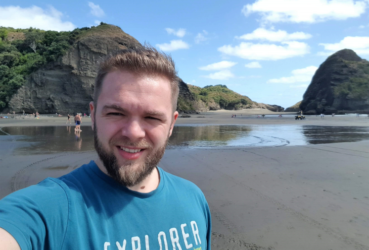 A young man takes a photo during a beach trip in New Zealand