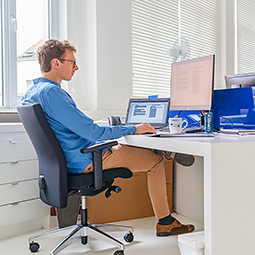 A young man sits in a desk chair and works with a computer