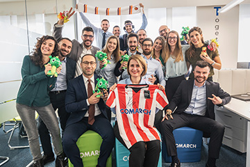 A group of people sitting in the office and holding a football jersey with the comarch company logo