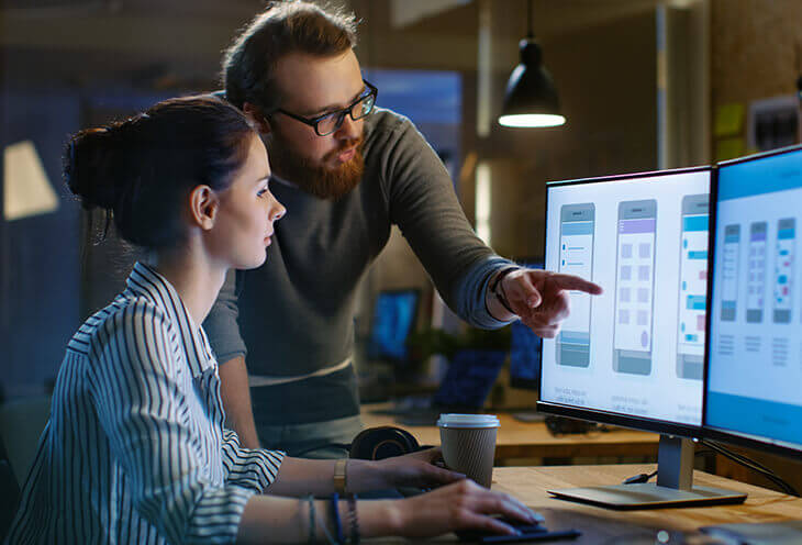 The man gives constructive criticism to his colleague at work. He shows her data on the monitor