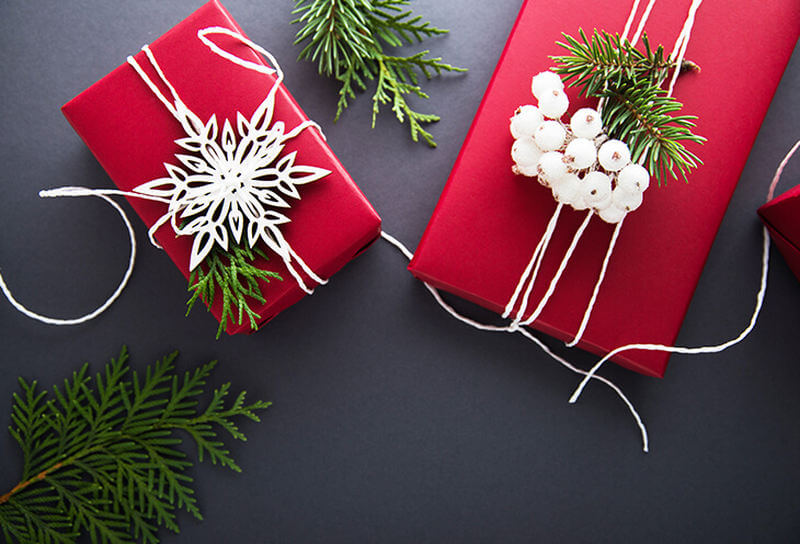 Two Christmas gifts decorated with a white ribbon. There is a Christmas tree scattered around