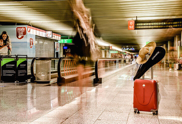 A red suitcase standing at the train station. On the handle hangs a pallet with the Comarch logo. 