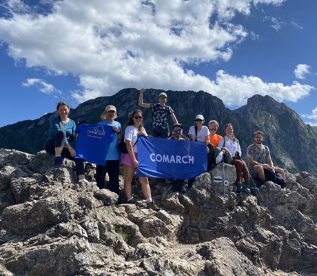 People standing on the top of the mountain holding Comarch logo.