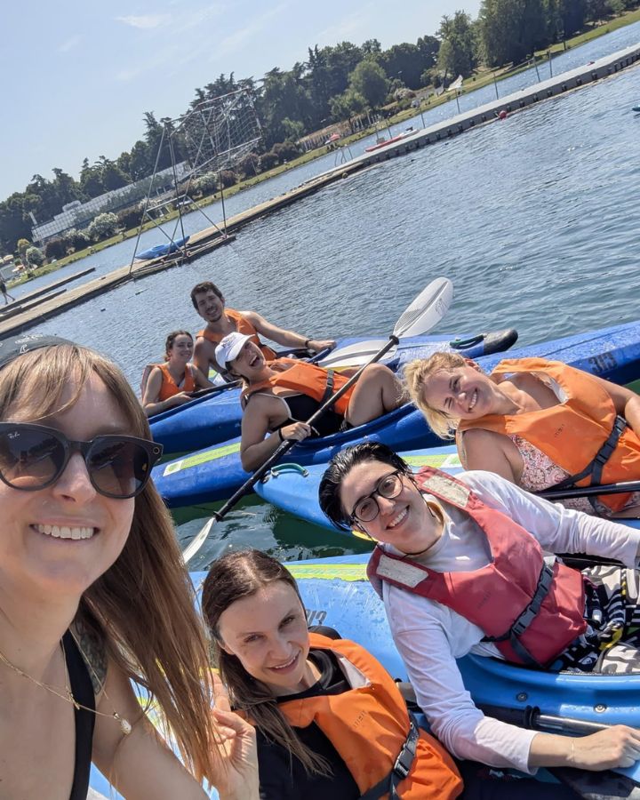 A group of smiling employees in life jackets enjoying a kayaking trip on a sunny lake during a company integration event.