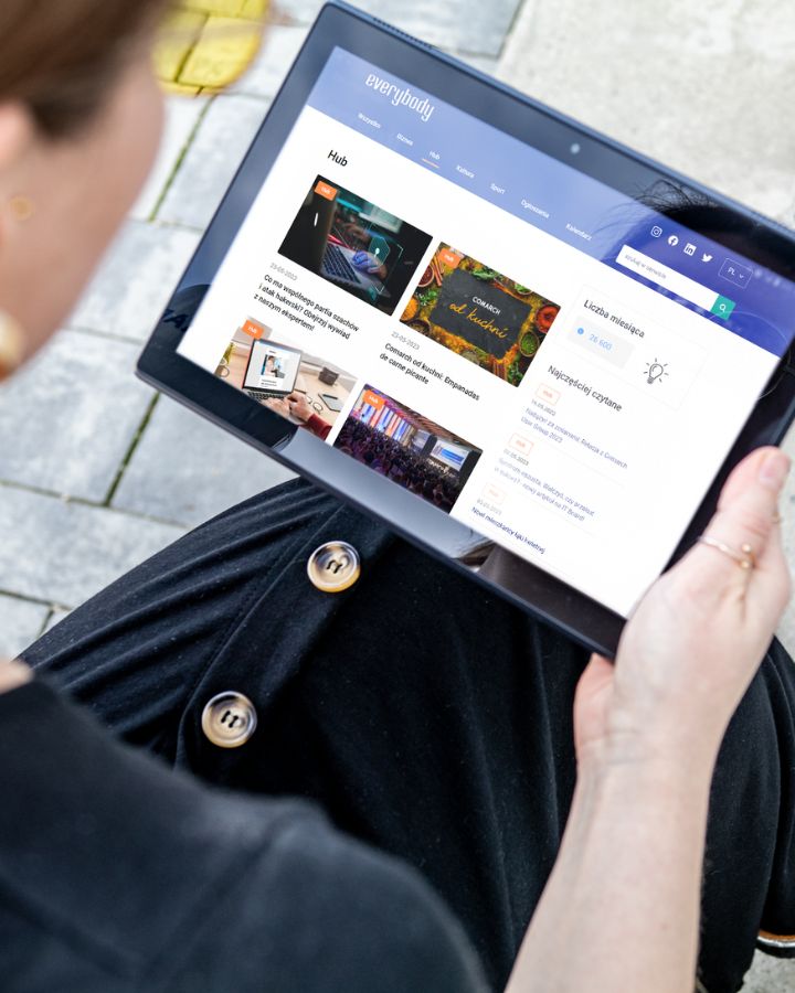 A close-up of a person holding a tablet displaying "Everybody," Comarch’s internal communication platform with news and company updates
