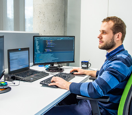 The man sits at the computer and works with three monitors
